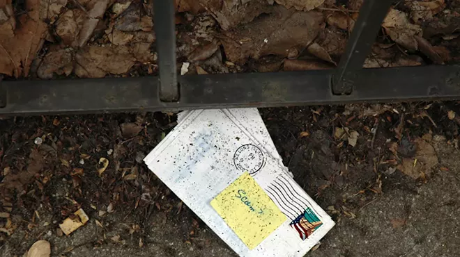 An envelope on the floor with a sticky note on top that reads "Scam?"