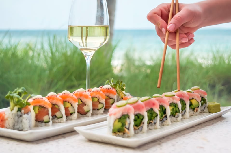 Image: sushi, a glass of wine, and a hand holding chopsticks