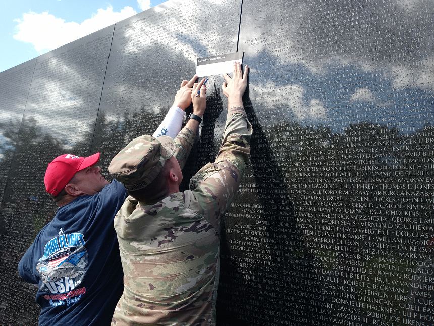 An Honor Flight guardian assists a servicemember etching the name of a fallen soldier from the Vietnam War onto a sheet of wax paper. - PHOTO BY JOSHUA CEBALLOS