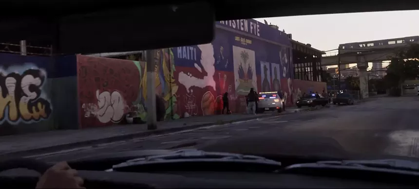 video game screenshot of a street scene featuring a mural with Haitian iconography