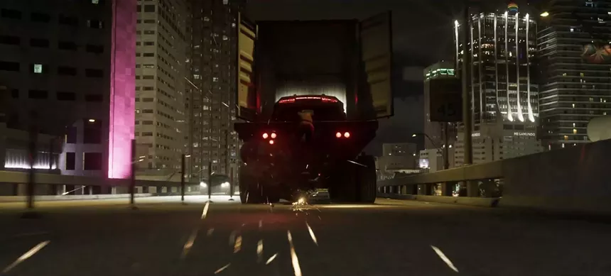 video game screenshot showing a car on the back of a flatbed truck entering a downtown area that can only be Miami, Florida